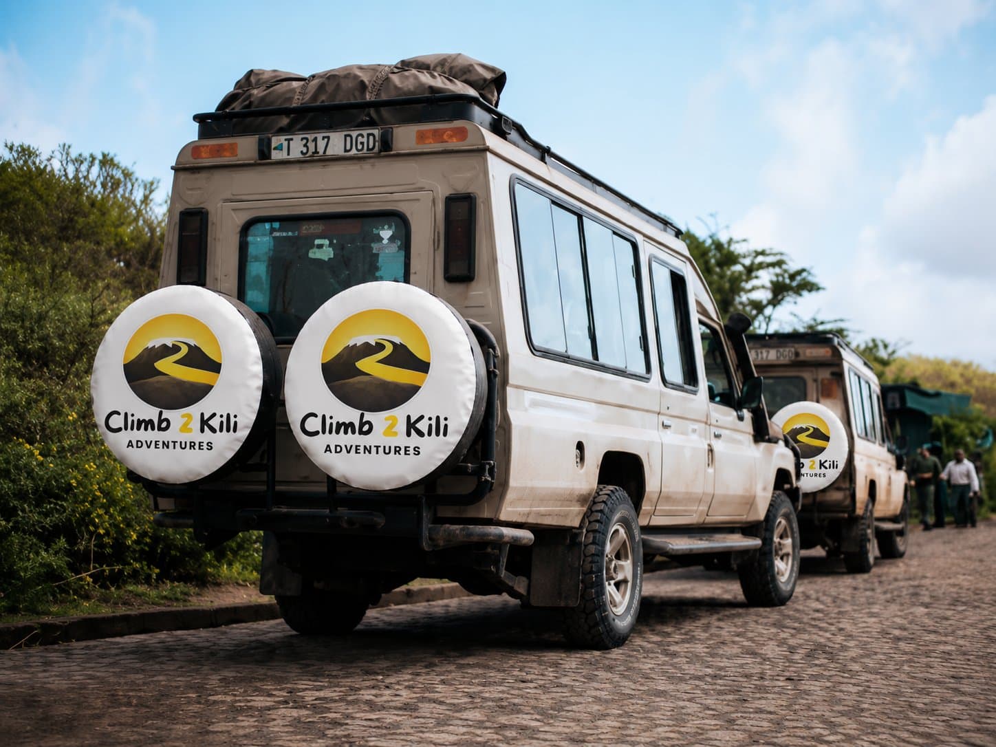 Gründer steht mit Kilimanjaro Führer, Träger, Köche, Fahrer und lokale Gemeindemitglieder unter dem Mount Kilimanjaro